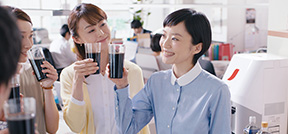 写真 職場 笑顔 みんながコーヒーを囲んでいる